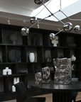 Modern chandelier hanging above a table with decorative vases in a room with bookshelves.