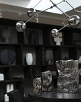 Modern chandelier hanging above a table with decorative vases in a room with bookshelves.