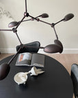 A modern chandelier hanging from the ceiling on a dining table styled with coffee table books and bowls.