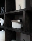 Dark wooden shelves with various white ceramic vases and objects against a black background