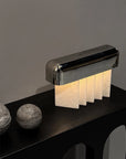 Modern table lamp with a metallic base and crystalized marble panels on a dark surface.