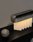 Modern table lamp with a metallic base and crystalized marble panels on a dark surface.