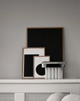 Framed artworks on a shelf against a gray wall with a textured surface.