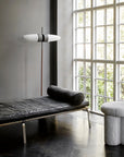 Modern interior with a black leather bench, gray ottoman, and floor lamp near a large window.