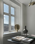Modern interior with a window, books, and a minimal sculptural vase on a table.