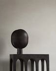 Dark metal sculptural table lamp with spherical top on a plain background