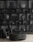 Collection of black sculptures and objects on shelves in a dark room.