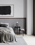 Modern bedroom with gray bedding, abstract art on the wall, and a side table.