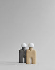 Two abstract Scandinavian human-like sculptural table lamps in gray and beige on a light gray background