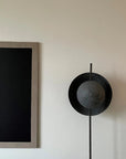 Modern floor lamp with black circular design on a white wall next to framed artwork.
