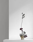 Minimalist flower arrangement in a small pot on a white surface with a gray background from 101 Copenhagen at Spacio retail stores in Mumbai & Kolkata.
