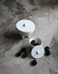 White ceramic containers with lids on a stone surface with blackberries from 101 Copenhagen at Spacio retail stores in Mumbai & Kolkata.