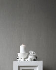 White candle and decorative items on a gray pedestal against a gray wall from 101 Copenhagen at Spacio retail stores in Mumbai & Kolkata.
