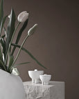 White tulips in a vase with three small white bowls on a stone surface against a brown background from 101 Copenhagen at Spacio retail stores in Mumbai & Kolkata.