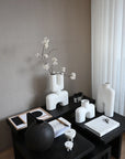 Decorative table with white and black vases, a flower arrangement, and stationery on a neutral background from 101 Copenhagen at Spacio retail stores in Mumbai & Kolkata.