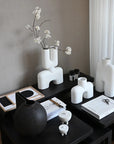 Decorative table with white and black vases, a flower arrangement, and stationery on a neutral background from 101 Copenhagen at Spacio retail stores in Mumbai & Kolkata.