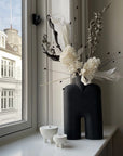 Decorative vase with flowers on a windowsill with cityscape view