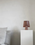 Ceramic vase from 101 Copenhagen on a white pedestal against a plain wall with a gray sofa.