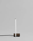 Minimalist table lamp with a white cylindrical shade and wooden base on a gray background