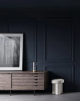 Dark blue paneled wall with a wooden sideboard and abstract art