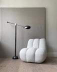 White textured chair and black floor lamp against a gray wall.