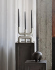 Modern candle holder with three black candles on a dark surface against a light curtain background from 101 Copenhagen at Spacio retail stores in Mumbai & Kolkata.