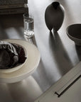 Table setting with a bowl, glass of water, and vase on a reflective surface.