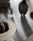 Table setting with a bowl, glass of water, and vase on a reflective surface.