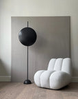 Modern black floor lamp next to a white textured armchair in a minimalistic room.