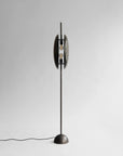 Side view of a modern floor lamp with a metallic base and cylindrical shade on a light gray background