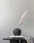 Black vase with dried plant on a table against a gray wall from 101 Copenhagen at Spacio retail stores in Mumbai & Kolkata.