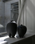 Two black ceramic vases on a windowsill with a building exterior in the background.