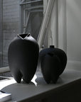 Two black ceramic vases on a windowsill with a building exterior in the background.