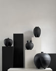 Black ceramic vases on white and black pedestals against a neutral background