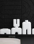 The white 101Cph Cobra Fat Medio Bubble White 201011 vase from 101 Copenhagen sits on a shelf in front of a black wall, showcasing the Cobra Arts Movement.