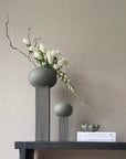 Two 101Cph Empire Mini Dark Grey 223036 ceramic vases by 101 Copenhagen, placed on a shelf alongside books and flowers.
