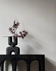 An organic-shaped 101Cph Cobra Double Mini Coffee 212002 vase sits on a table in an interior setting next to a white wall.