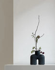 A quirky black vase, the 101Cph Cobra Uno Mini Black 203024 from 101 Copenhagen, gracefully adorns a pristine white wall.