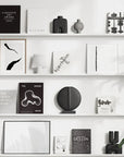 A white shelf with black and white art, a plant, and quirky 101Cph Guggenheim Mini Coffee 111220 vases.