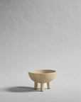 Beige ceramic bowl with three legs on a gray background from 101 Copenhagen at Spacio retail stores in Mumbai & Kolkata.