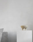 Small ceramic bowl on a white pedestal against a plain wall with a gray cushioned chair from 101 Copenhagen at Spacio retail stores in Mumbai & Kolkata.