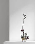 Minimalist flower arrangement in a small pot on a white surface with a gray background from 101 Copenhagen at Spacio retail stores in Mumbai & Kolkata.