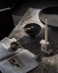 Table setting with a newspaper, cup of coffee, bowl, and candle on a dark marble surface from 101 Copenhagen at Spacio retail stores in Mumbai & Kolkata.