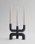 Black modern candle holder with three candles on a gray background from 101 Copenhagen at Spacio retail stores in Mumbai & Kolkata.