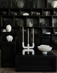 Modern candle holder with white base and black candles on a dark surface with shelves in the background from 101 Copenhagen at Spacio retail stores in Mumbai & Kolkata.