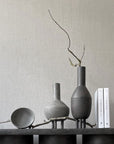 A 101Cph Duck Fat Dark Grey 111281 table adorned with vases and books, embracing the Cobra Arts Movement aesthetic. (Brand Name: 101 Copenhagen)