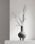 A 101Cph Duck Fat Dark Grey 111281 vase from 101 Copenhagen sits on top of a white pedestal.