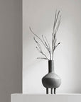 A 101Cph Duck Fat Dark Grey 111281 vase from 101 Copenhagen sits on top of a white pedestal.