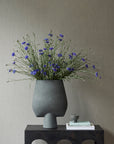 Gray vase with purple flowers on a dark surface against a gray wall from 101 Copenhagen at Spacio retail stores in Mumbai & Kolkata.