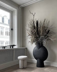 A black 101 Copenhagen vase sits next to a window in a room.